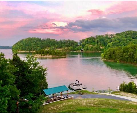 A lake cove at sunset with a covered boat dock below the lawn
