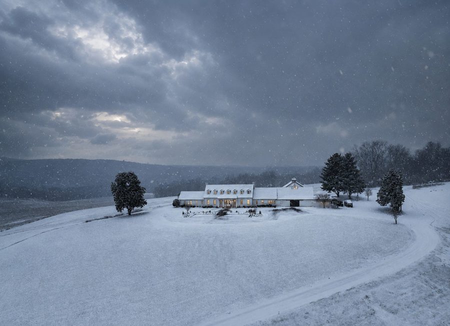 The estate under snowfall at dusk, windows lit