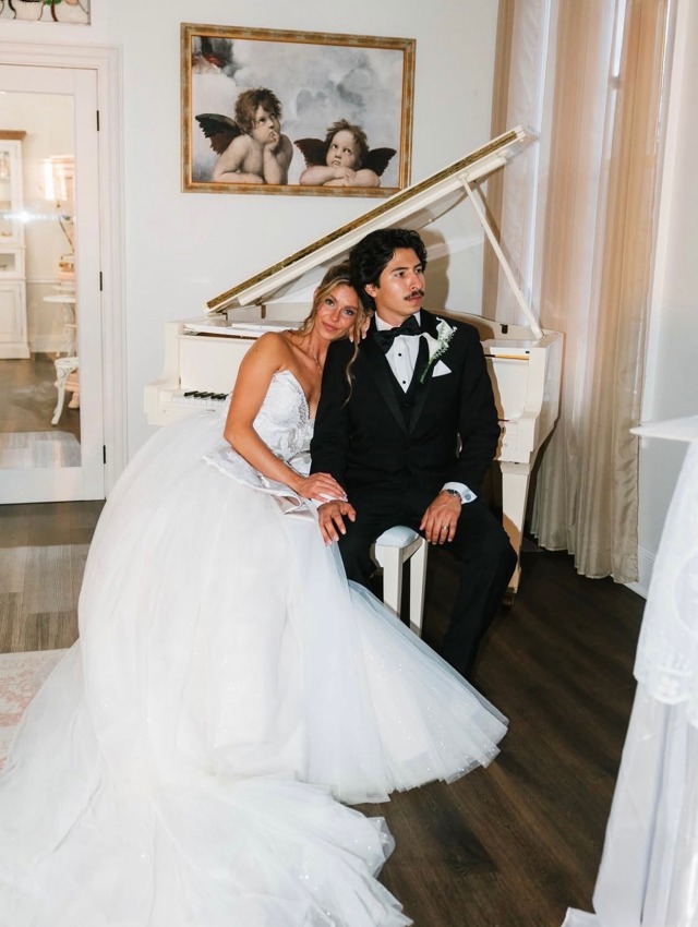 A bride and groom at the white grand piano beneath the cherub painting
