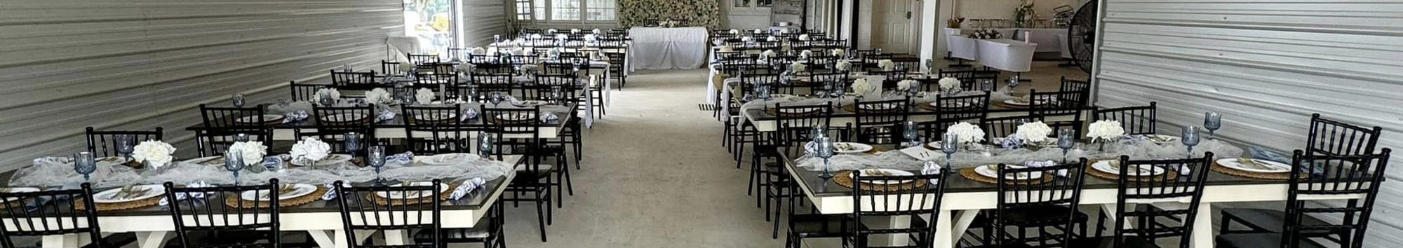 Long tables set for dinner in the pavilion, chargers and glassware down both sides
