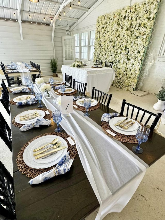 A long table laid with gold chargers and blue glassware