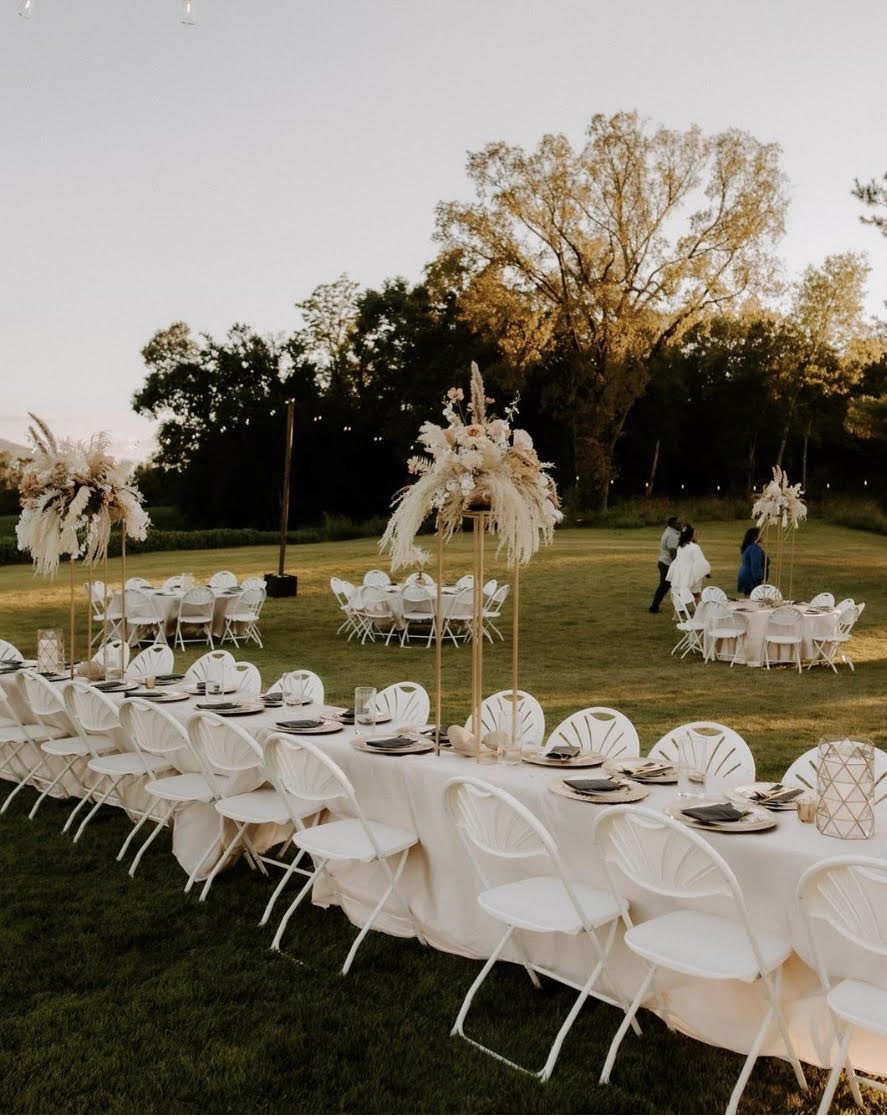 A long table set out on the grass at dusk, guests gathering beyond