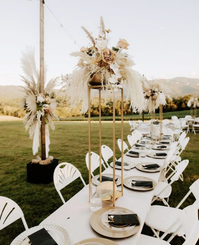 A long table set on the lawn at dusk, dried florals down the centre